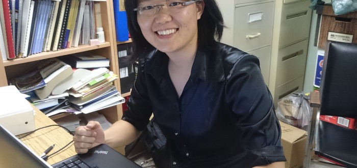 Woman smiling at her desk with a computer keyboard and bookshelves.